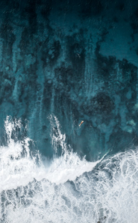 Aerial view of surf breaking along a dark shoreline