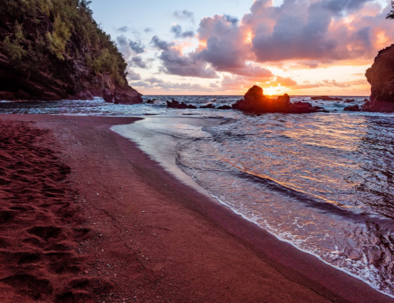 Waves washing over a dark-sand beach at sunset